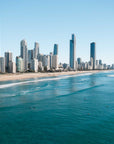 Surfers sitting in turquoise water off Surfers Paradise beach with the Gold Coast skyline and Q1 tower behind them