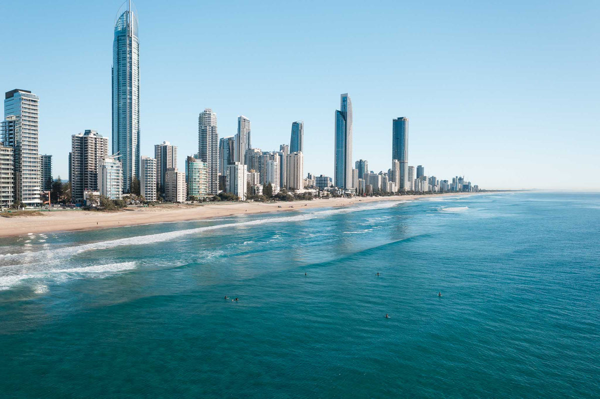 Surfers sitting in turquoise water off Surfers Paradise beach with the Gold Coast skyline and Q1 tower behind them