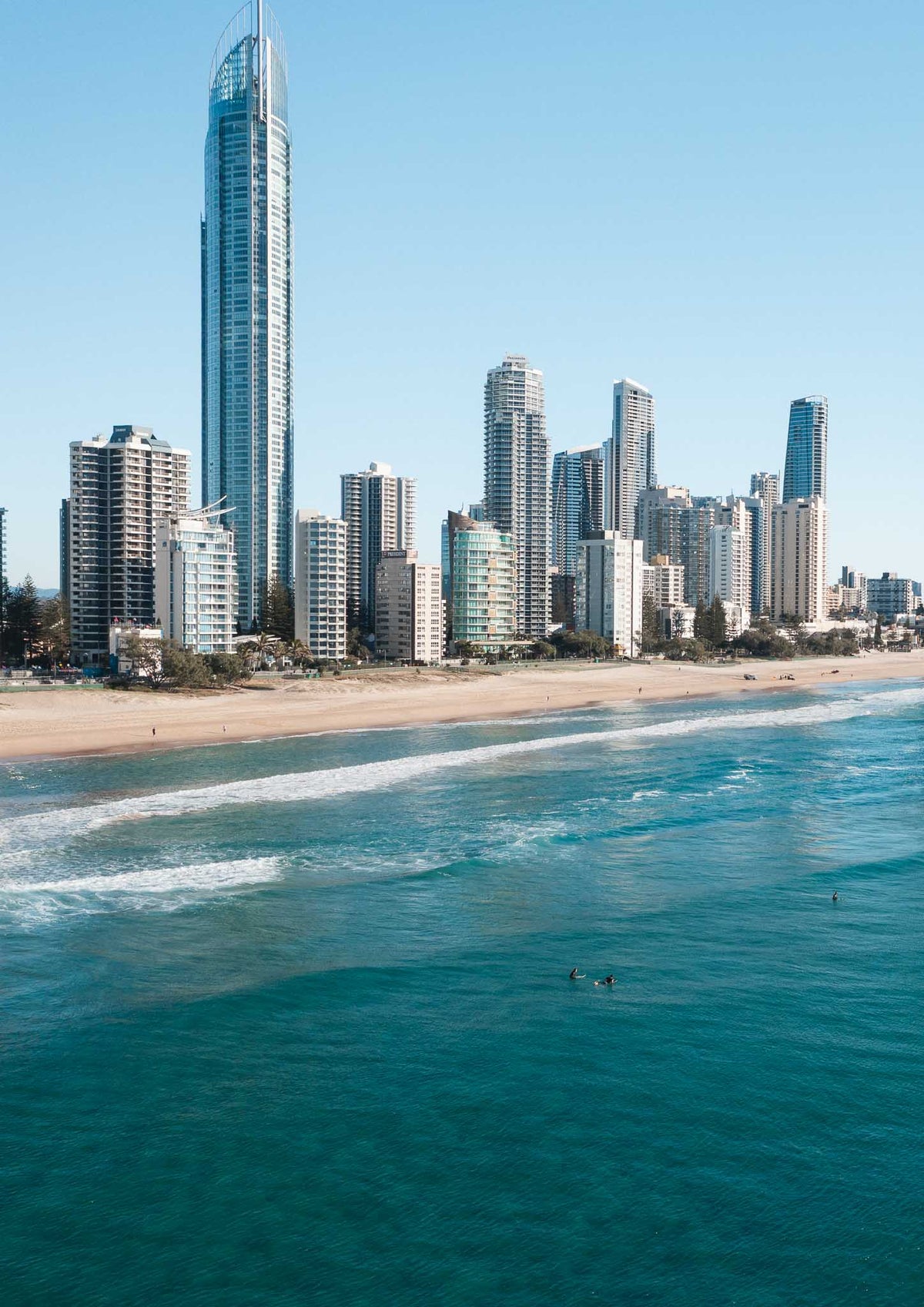 Surfers sitting in turquoise water off Surfers Paradise beach with the Gold Coast skyline and Q1 tower behind them