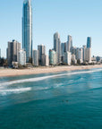 Surfers sitting in turquoise water off Surfers Paradise beach with the Gold Coast skyline and Q1 tower behind them