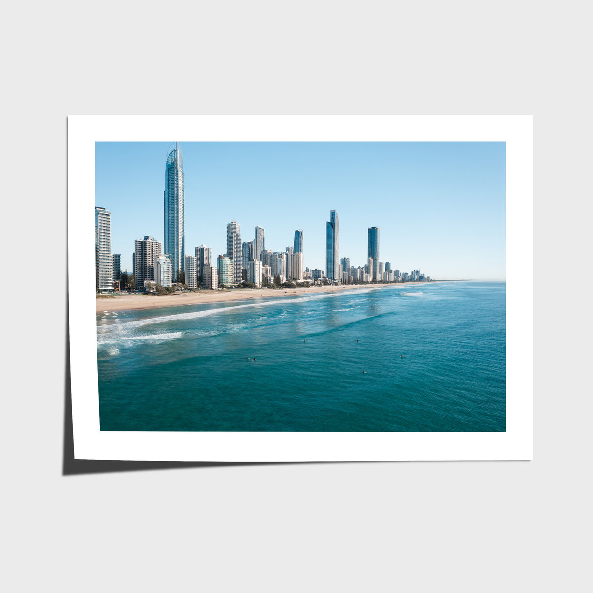 Surfers sitting in turquoise water off Surfers Paradise beach with the Gold Coast skyline and Q1 tower behind them