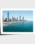 Surfers sitting in turquoise water off Surfers Paradise beach with the Gold Coast skyline and Q1 tower behind them